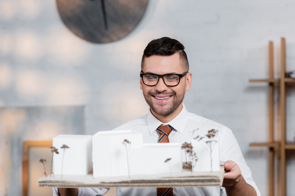 cheerful architect in eyeglasses holding buildings maquette in architectural agency - Photo, Image