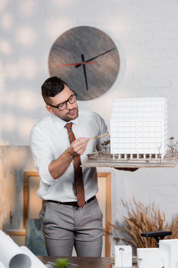 arkkitehti silmälasien seisoo työpaikalla ja osoittaa lyijykynällä talon maquette - Valokuva, kuva