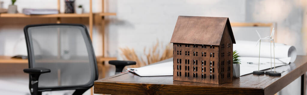 Hausmodell in der Nähe von Windkraftanlagen auf Schreibtisch im Architekturbüro, Banner - Foto, Bild