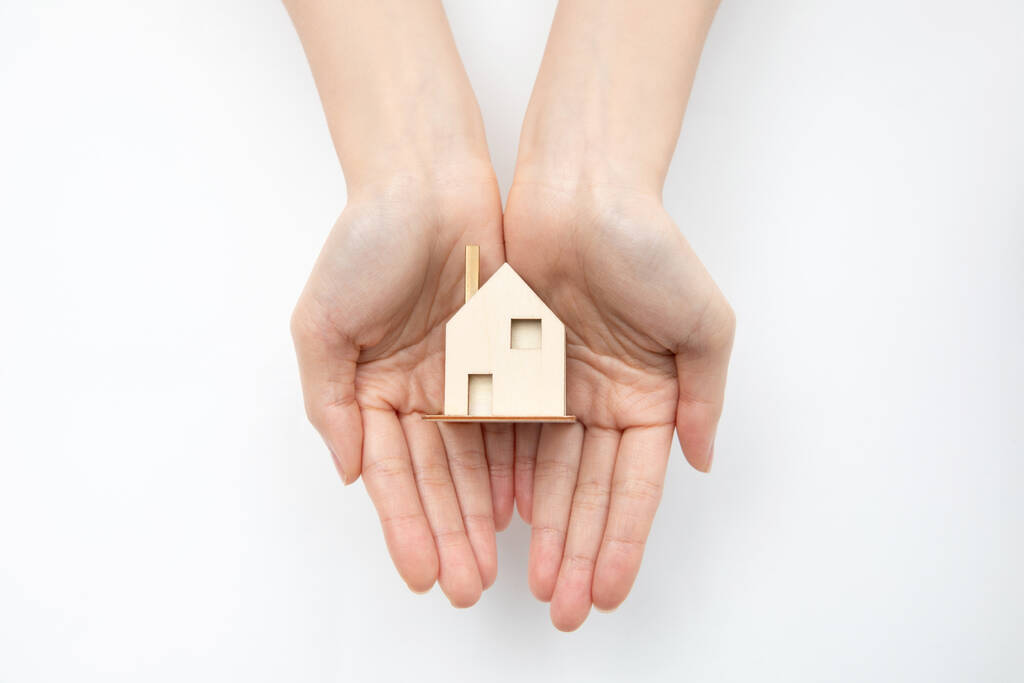 Uma vista superior das mãos segurando um conceito de casa-imobiliário de madeira pequena - Foto, Imagem