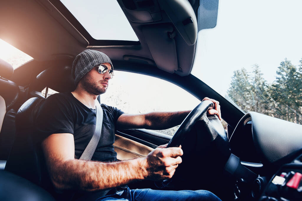 Un hombre con gafas y una camiseta negra conduce un coche con concentración: carreras callejeras - Foto, imagen