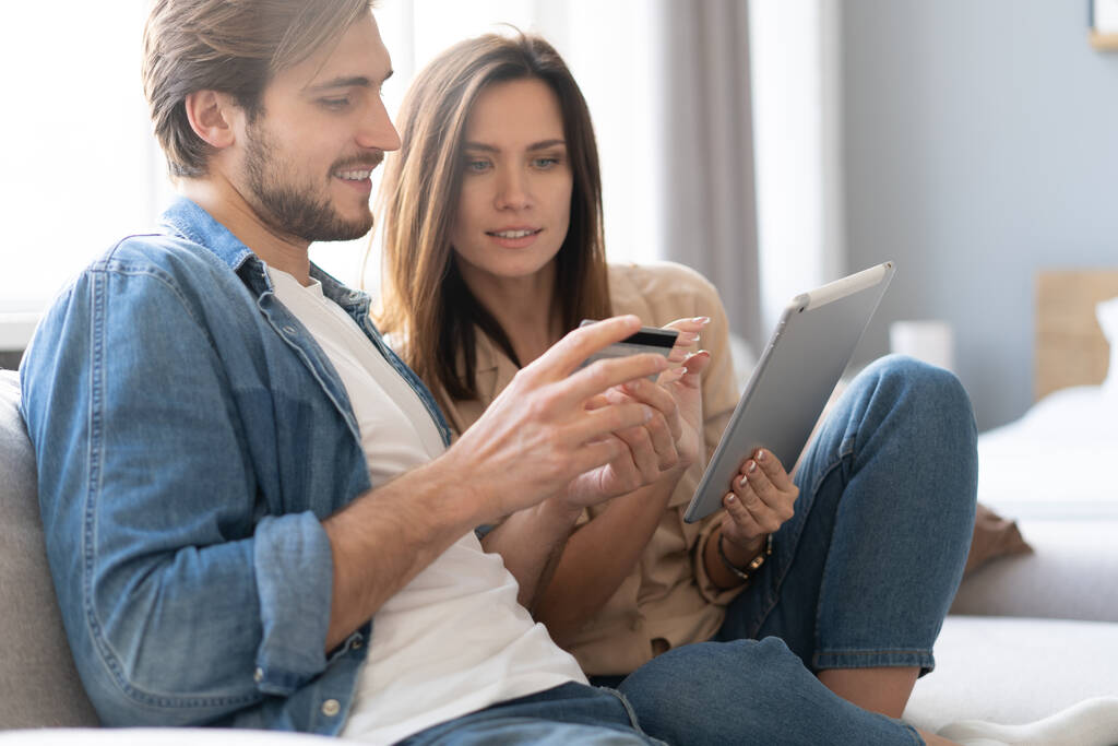 Couple riant assis sur le canapé faisant du shopping en ligne avec tablette PC à la maison dans le salon. - Photo, image