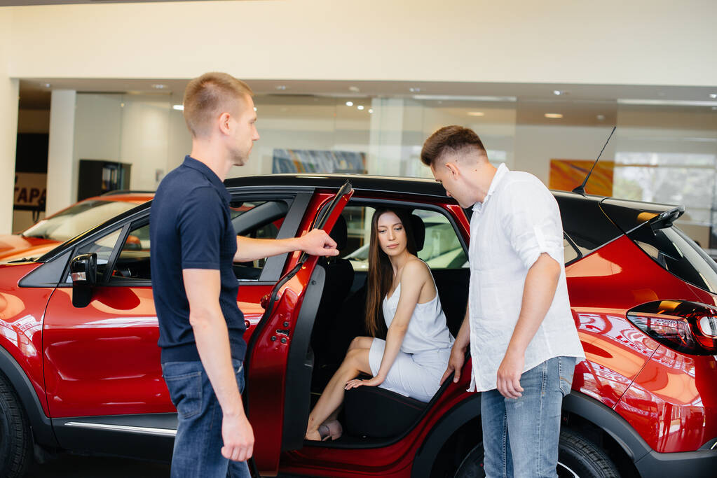 Una feliz pareja joven elige y compra un coche nuevo en un concesionario de automóviles. Comprar un coche nuevo - Foto, imagen