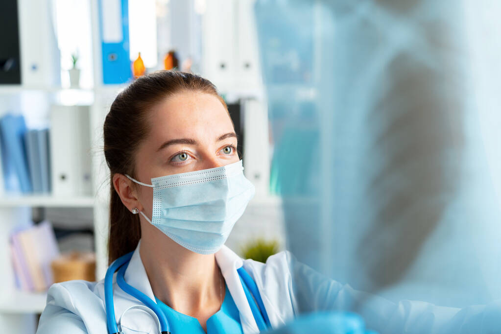 Femme médecin dans le masque médical examine la radiographie des poumons - Photo, image