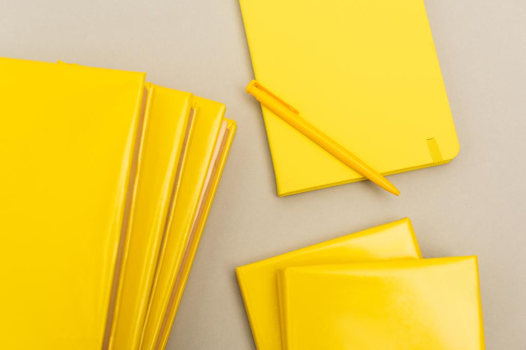 bovenaanzicht van gele notitieblokken bij pen geïsoleerd op grijs - Foto, afbeelding