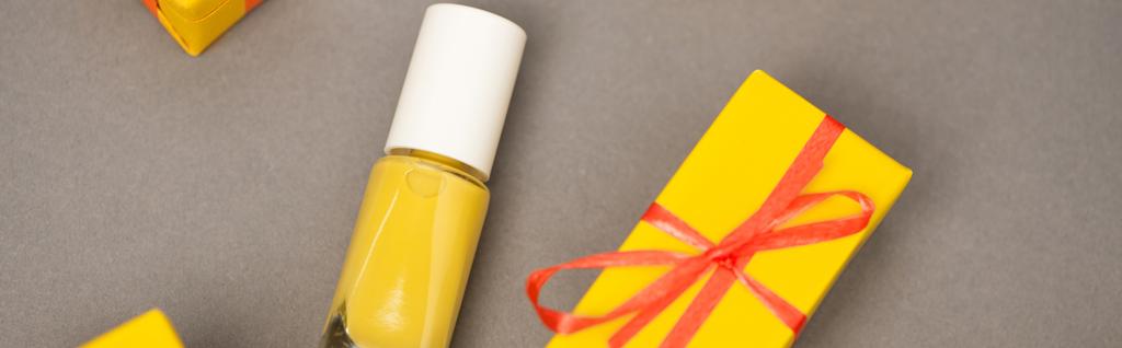 θέα υψηλής γωνίας του τυλιγμένο κίτρινο κουτί δώρου κοντά μπουκάλι με βερνίκι νυχιών σε γκρι, banner - Φωτογραφία, εικόνα