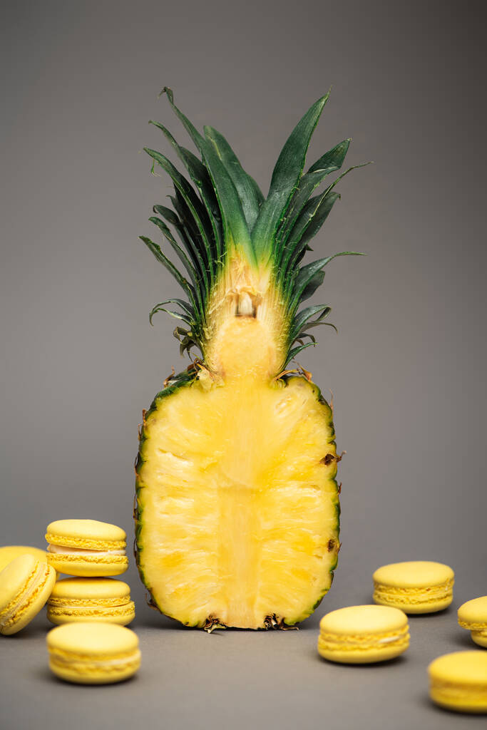 puolet kypsää ja tuoretta ananasta lähellä keltaisia makaroneja harmaalla  - Valokuva, kuva