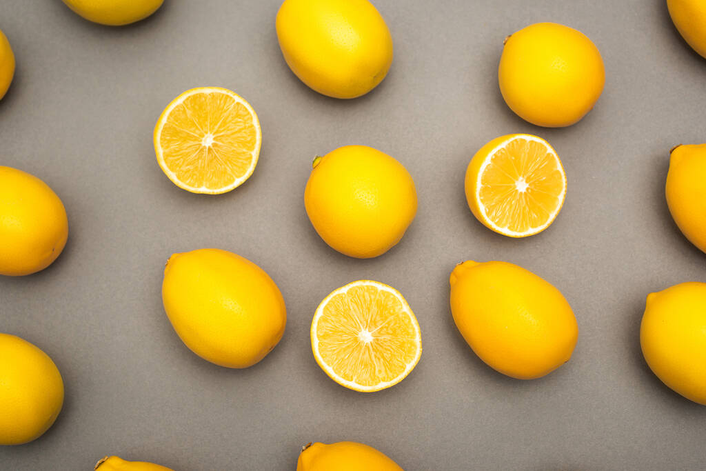 Gri arkaplanda sarı limonlar ve yarıların yüksek açılı görüntüsü - Fotoğraf, Görsel