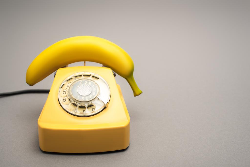 желтый банан на ретро-телефоне на сером фоне - Фото, изображение