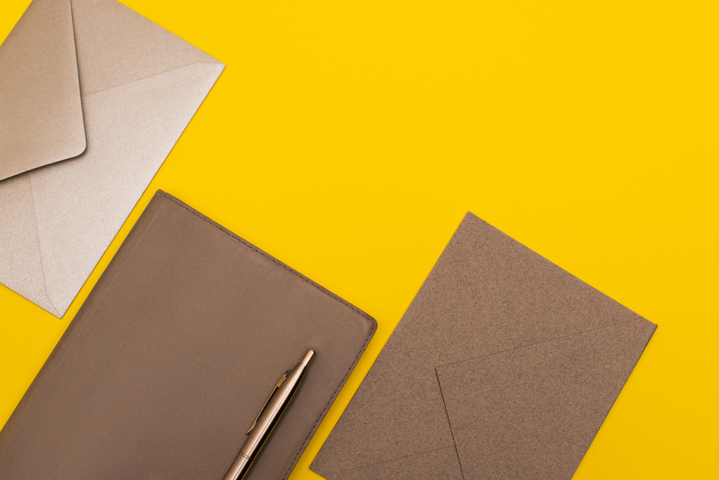 vista dall'alto di notebook con penna dorata vicino buste isolate su giallo - Foto, immagini