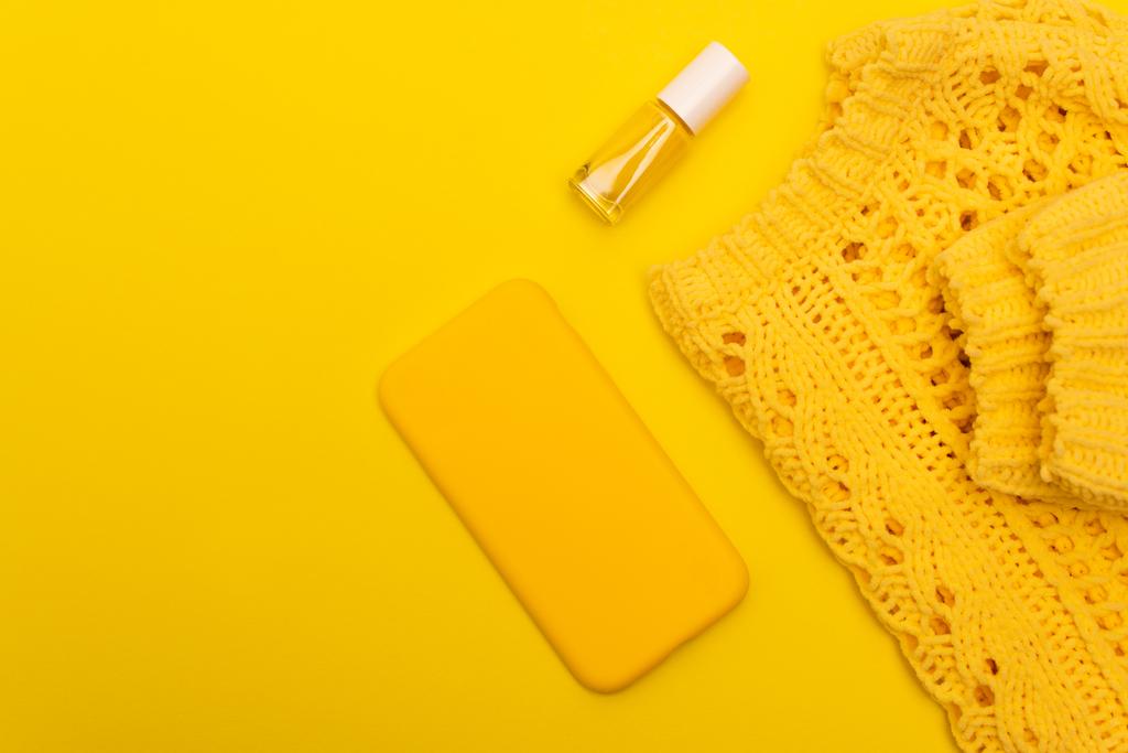 vrchní pohled na láhev s lakem na nehty, smartphone v případě, že v blízkosti jumper izolované na žluté  - Fotografie, Obrázek