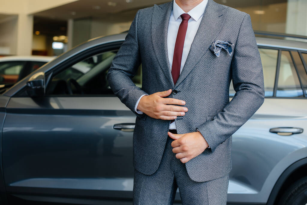 Un joven hombre de negocios mira un coche nuevo en un concesionario de automóviles. Comprar un coche - Foto, imagen