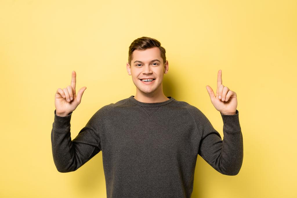 Cheerful man pointing up with fingers and looking at camera on yellow background - Photo, Image