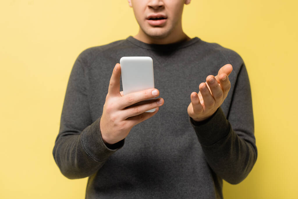 Cropped view of man pointing with hand while using smartphone on yellow background - Photo, Image