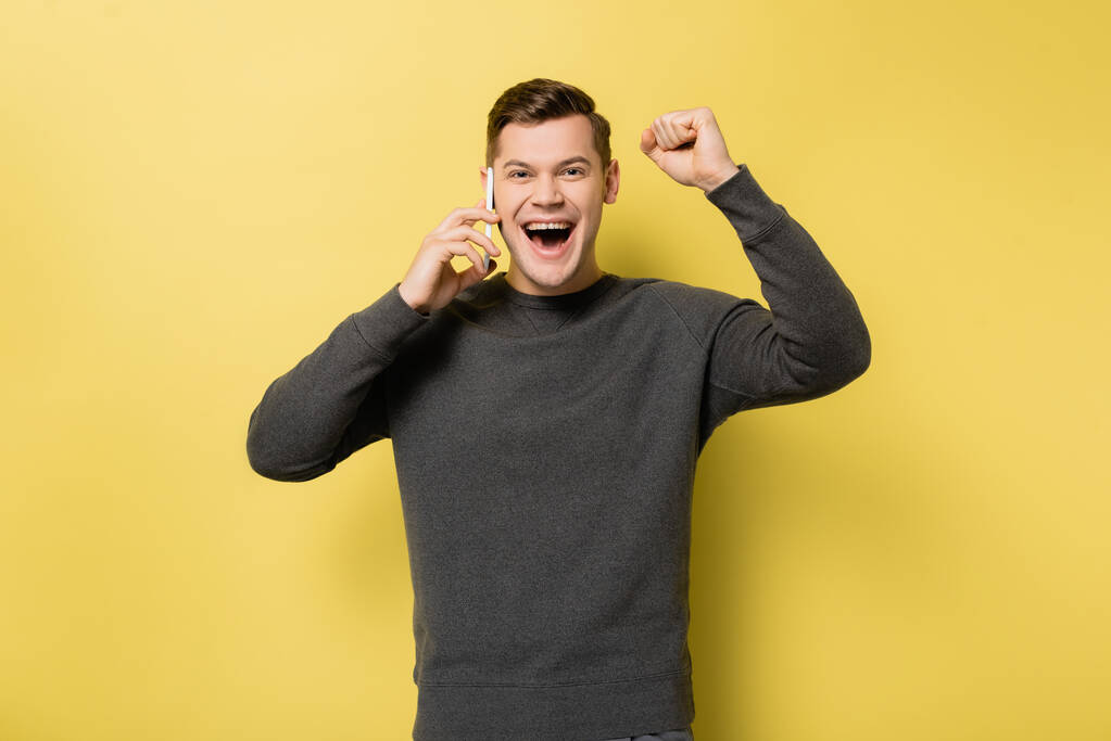 Excited man talking on smartphone and showing yes gesture on yellow background - Photo, Image