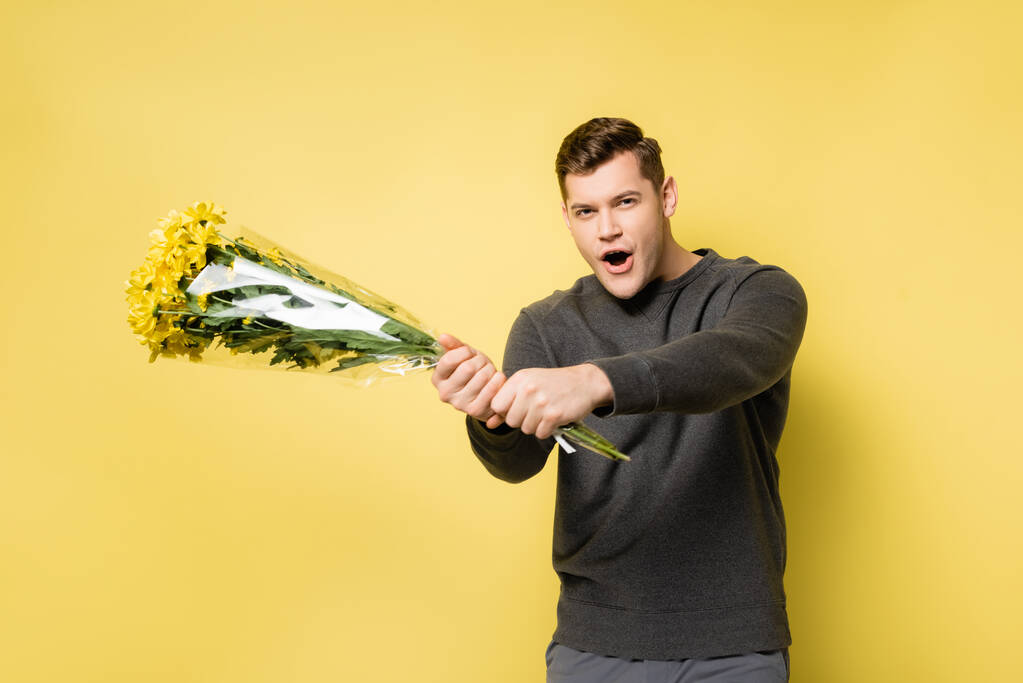 Excited man holding bouquet on yellow background - Photo, Image