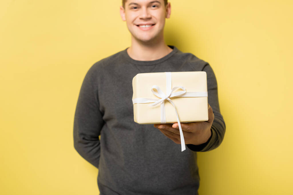 Geschenkbox in der Hand eines lächelnden Mannes verschwommen auf gelbem Hintergrund - Foto, Bild