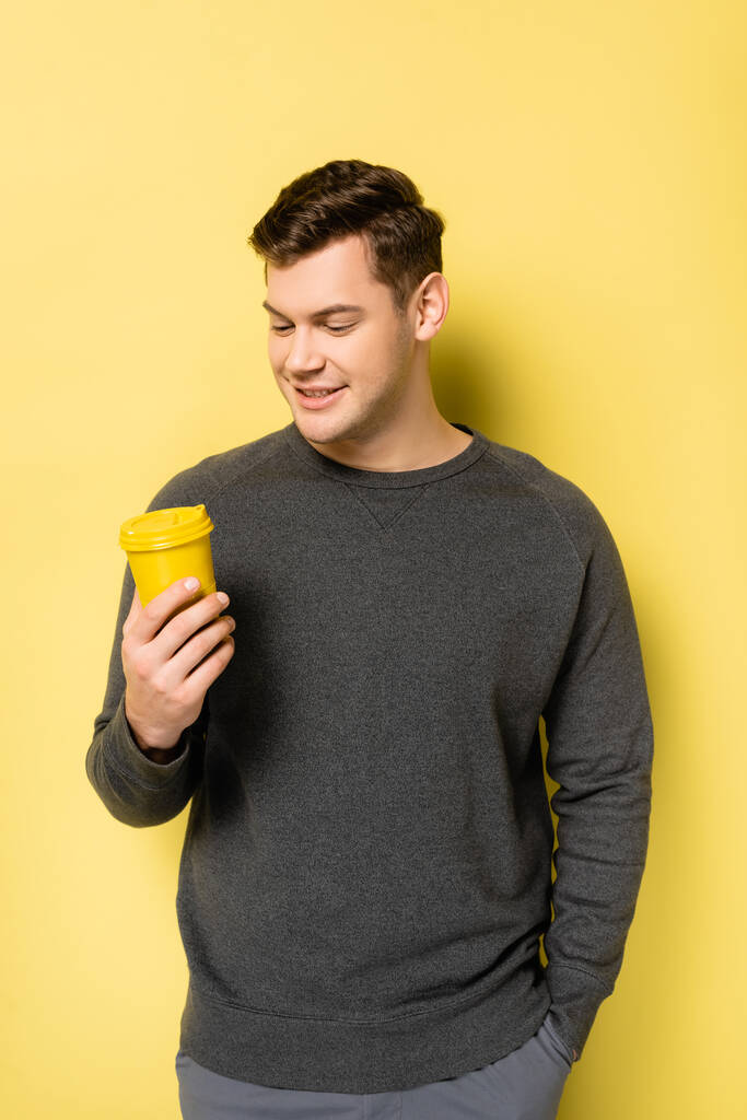 Uśmiechnięty mężczyzna trzymający kawę na żółtym tle - Zdjęcie, obraz