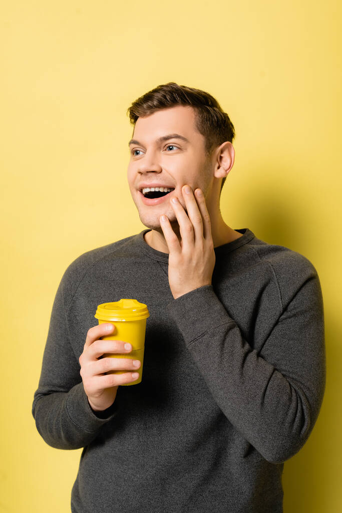 Θετικός άνθρωπος κρατώντας καφέ για να πάει στο κίτρινο φόντο - Φωτογραφία, εικόνα