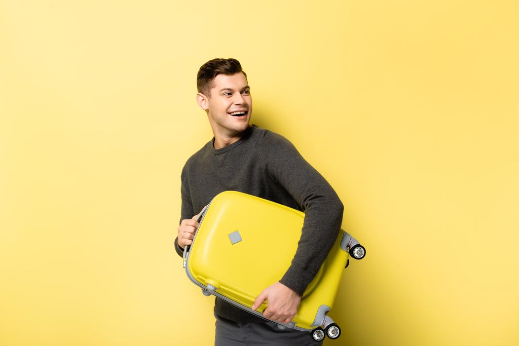 Smiling man holding baggage on yellow background - Photo, Image