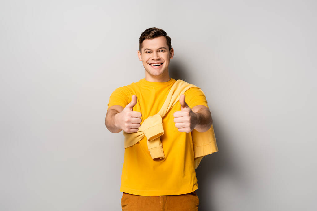 Χαμογελαστή άνθρωπος δείχνει αντίχειρες επάνω σε γκρι φόντο  - Φωτογραφία, εικόνα