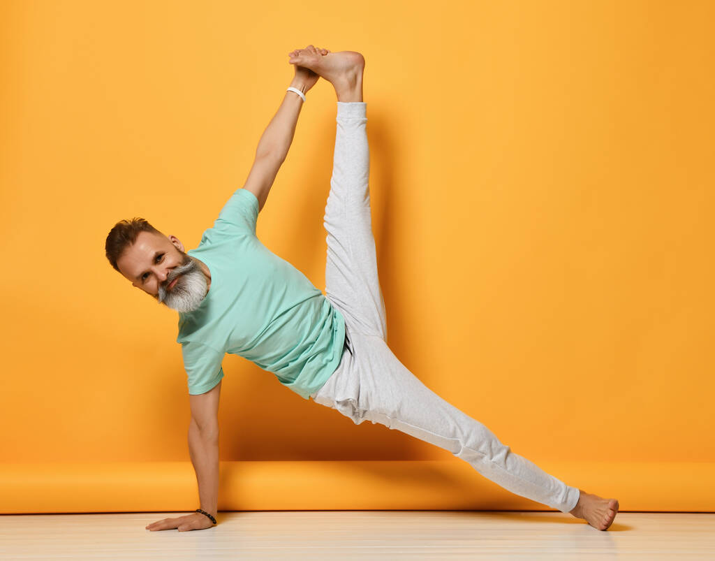 Glimlachende man met baard met grijs haar oefent yoga les studio shot - Foto, afbeelding