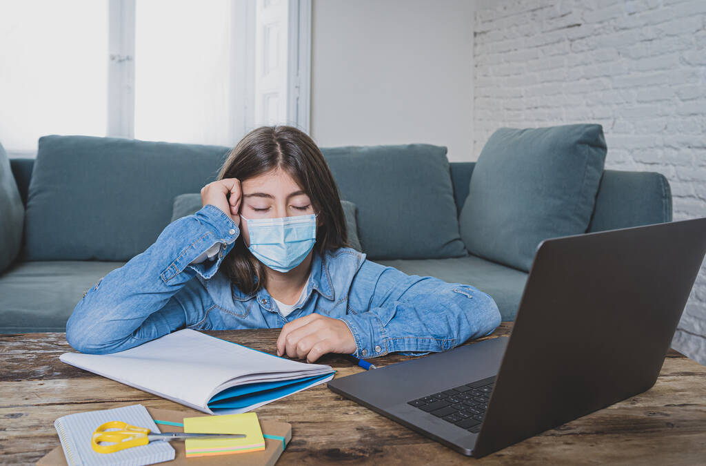 Nudná a deprimovaná dospívající dívka s obličejovou maskou na notebooku studující doma v online třídě jako střední škola zůstává zavřená z důvodu uzamčení nového COVID-19 nebo předpovědi počasí. - Fotografie, Obrázek