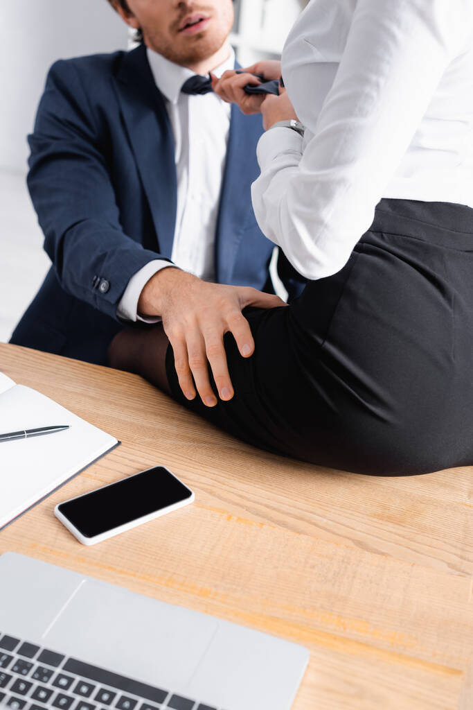 vista recortada de la mujer de negocios sentada en el escritorio mientras seduce a su colega en la oficina - Foto, imagen