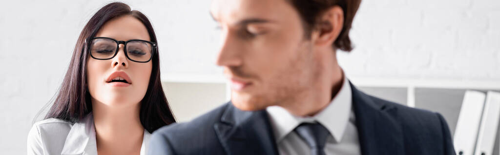 apasionada secretaria morena en gafas cerca de joven hombre de negocios en primer plano borrosa, pancarta - Foto, imagen