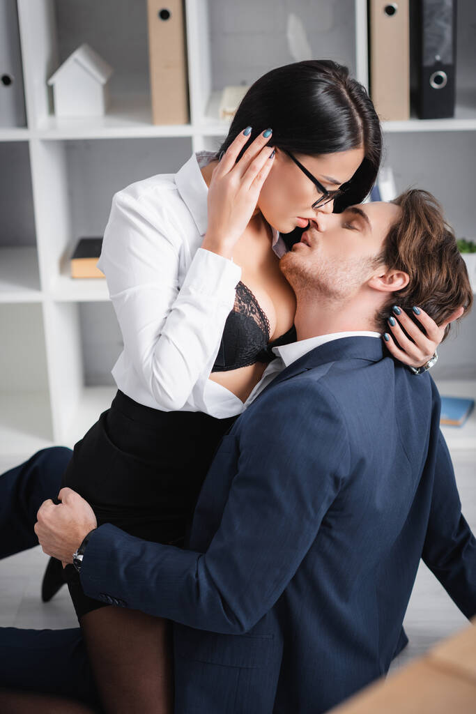sexy morena mujer de negocios besando joven colega en piso en la oficina - Foto, Imagen