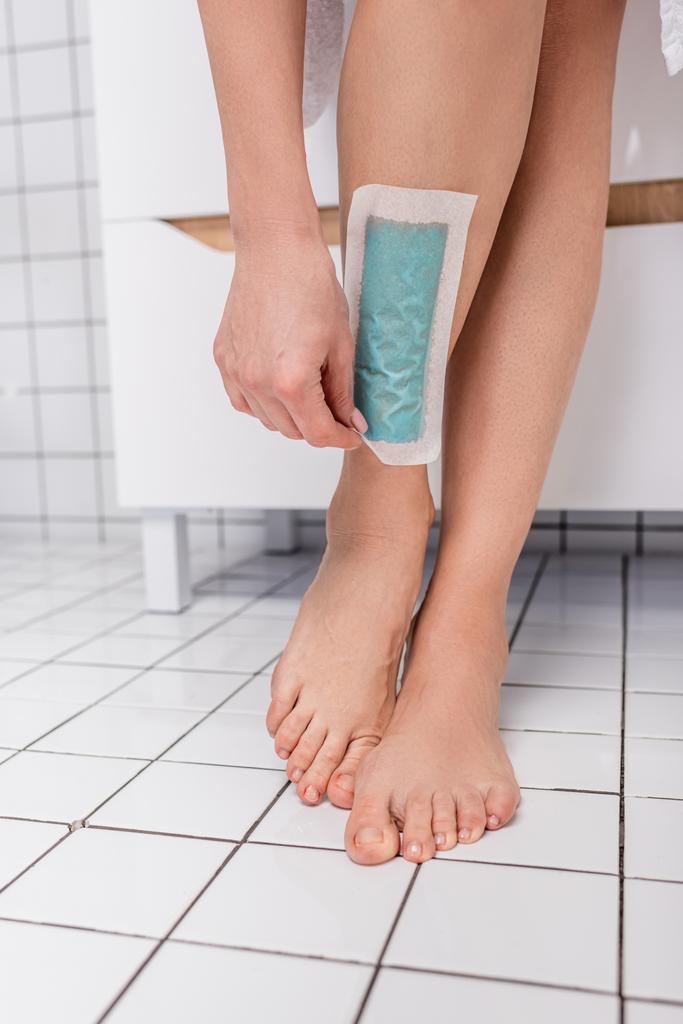 Banyoda balmumu şeritli bacağını kesen kadının görüntüsü. - Fotoğraf, Görsel