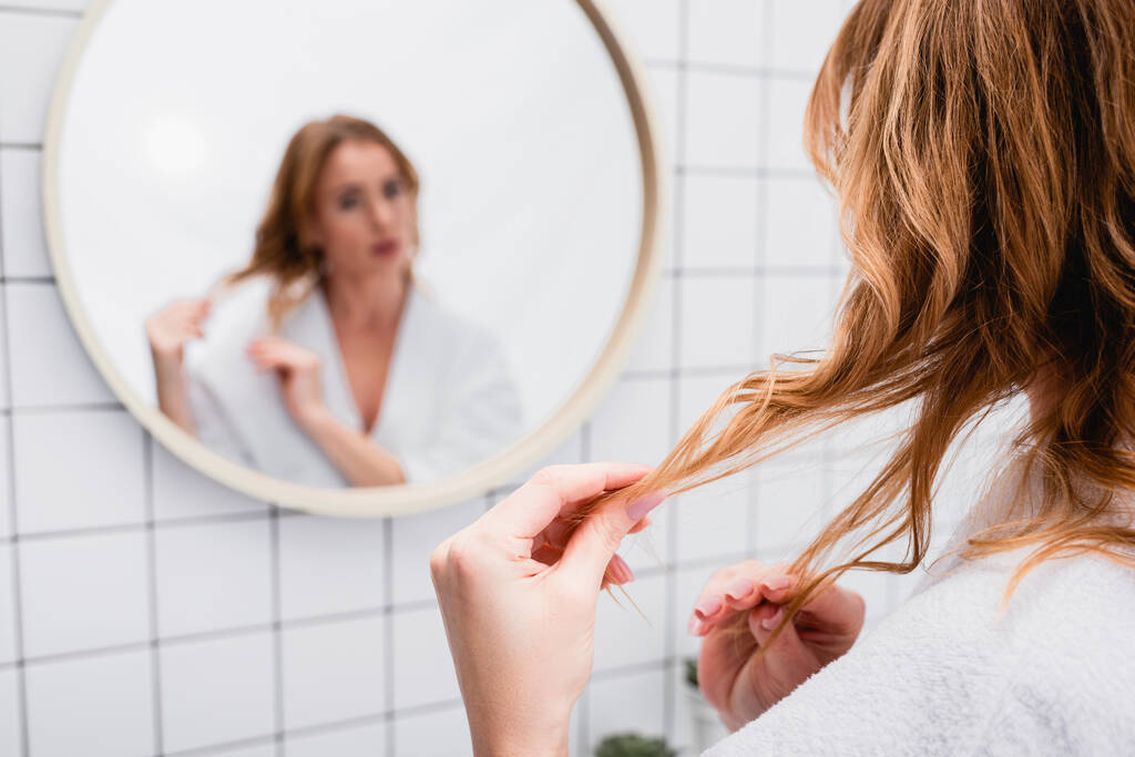 mujer ajustando el cabello cerca del espejo sobre fondo borroso - Foto, imagen