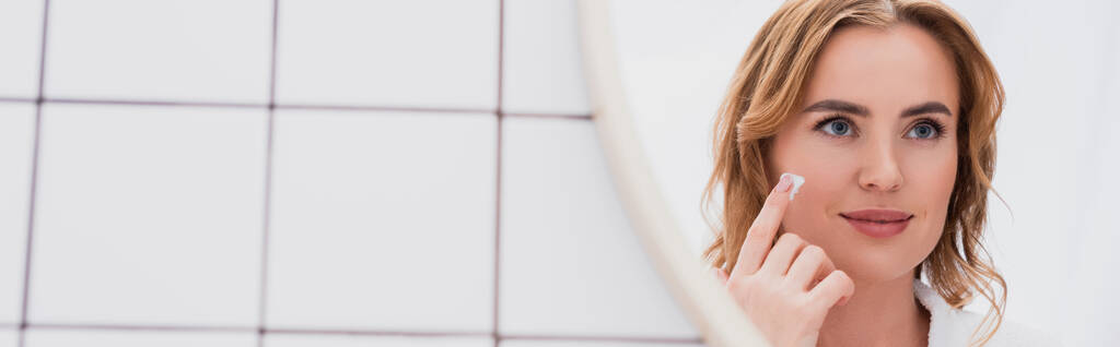 鏡を見ながら顔クリームを塗る幸せ女性バナー - 写真・画像