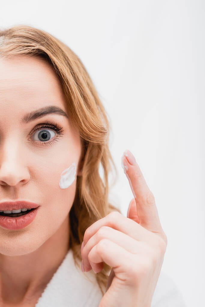 částečný pohled na překvapenou ženu s kosmetickým krémem na obličeji v koupelně  - Fotografie, Obrázek