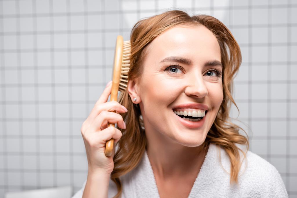 onnellinen nainen hymyilee ja harjaamalla hiukset kylpyhuoneessa - Valokuva, kuva