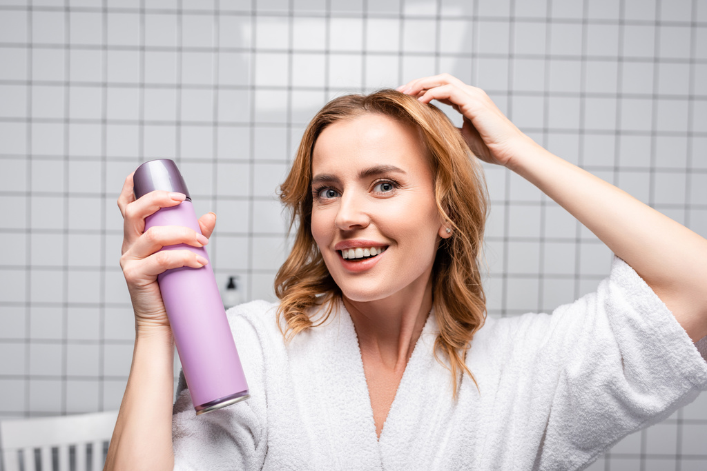 χαρούμενη γυναίκα κρατώντας μπουκάλι με σπρέι μαλλιών στο μπάνιο - Φωτογραφία, εικόνα