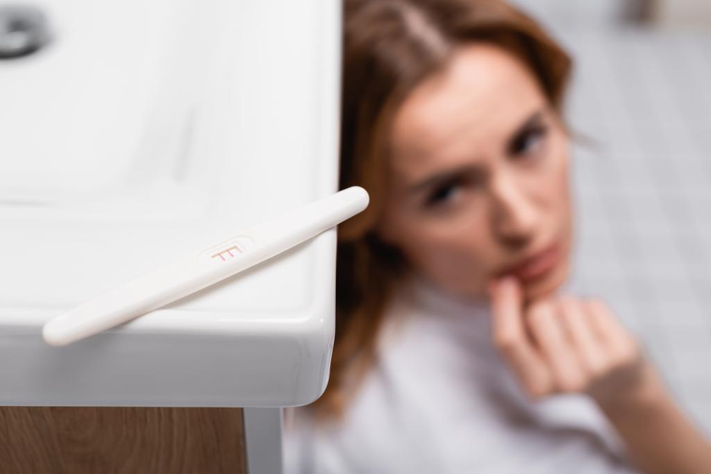 тест на беременность с положительным результатом рядом с обеспокоенной женщиной на размытом фоне - Фото, изображение