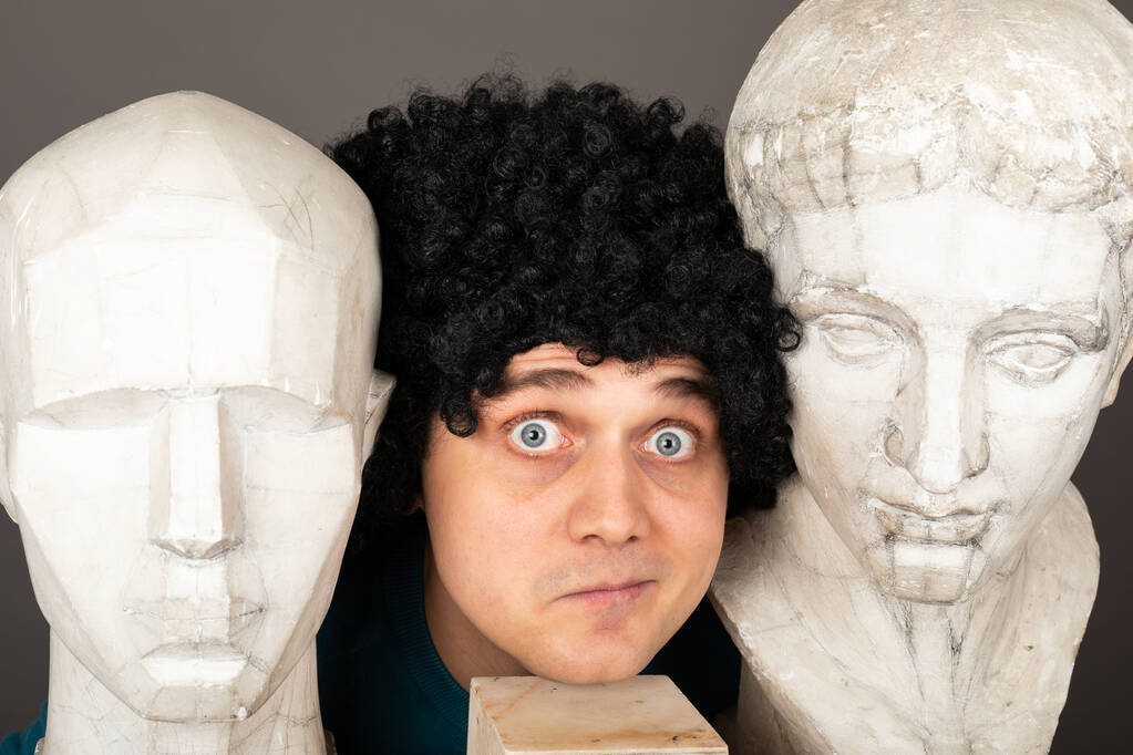 灰色の背景の前に石膏像を頭に持つ若い創造的な男性アーティストの肖像画 - 写真・画像