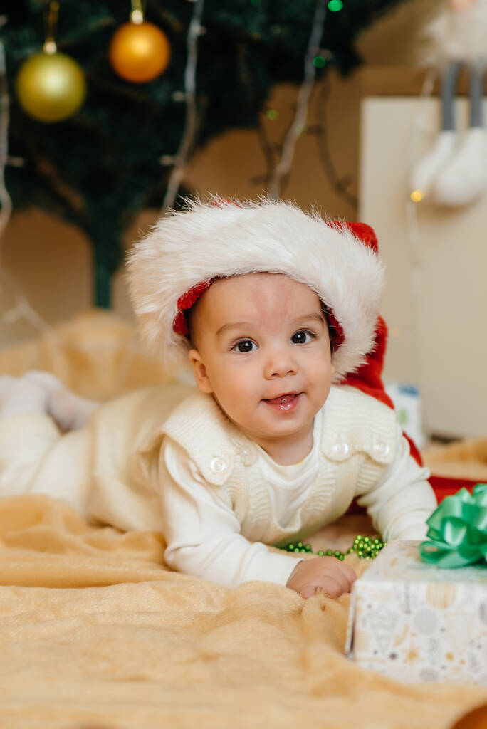 Schattige lachende baby ligt onder een feestelijke kerstboom en spelen met geschenken. Kerst- en nieuwjaarsviering - Foto, afbeelding