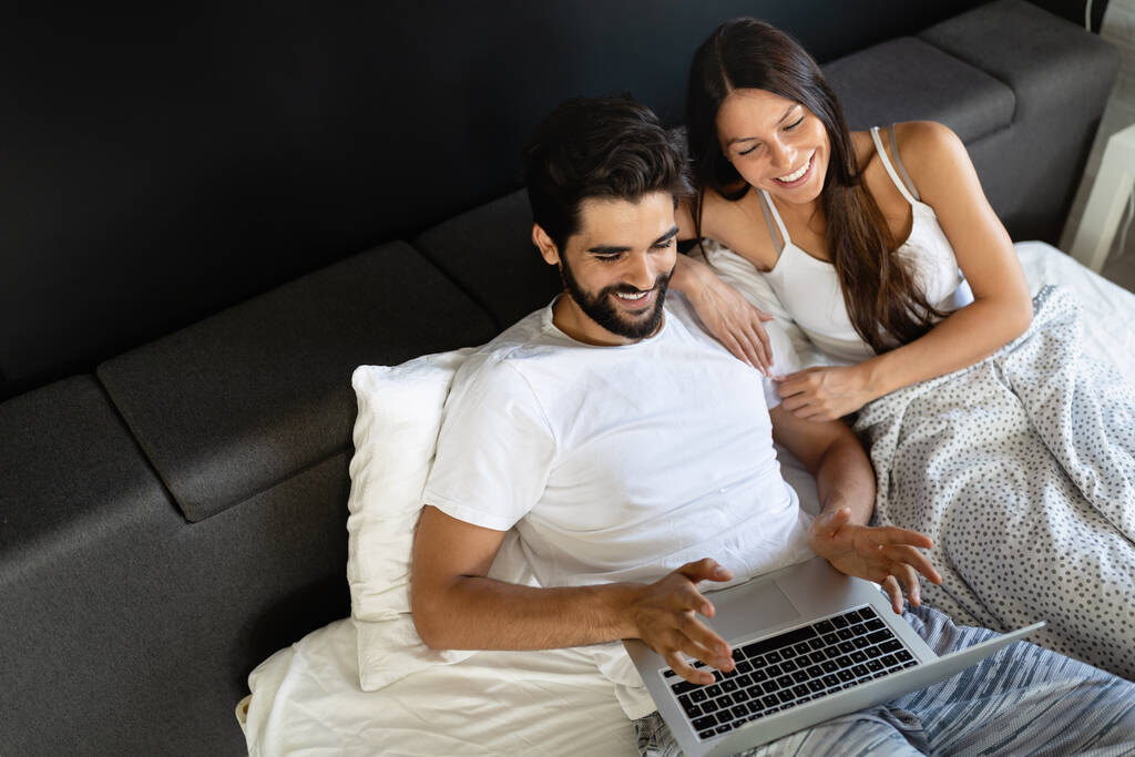 Joven feliz pareja sonriente con ordenador portátil en el dormitorio - Foto, Imagen