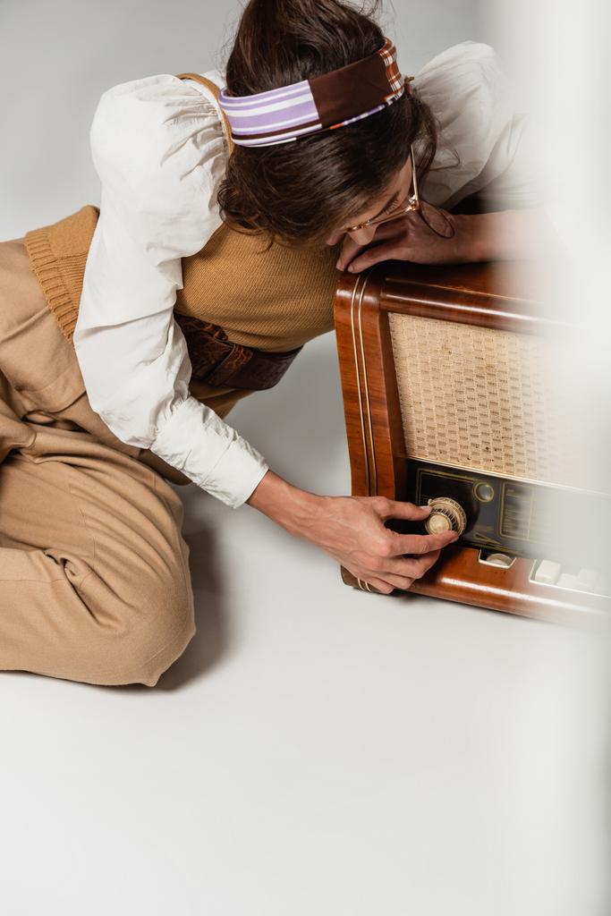Frau in Stirnband und Retro-Klamotten stellt Vintage-Radioempfänger auf grau - Foto, Bild