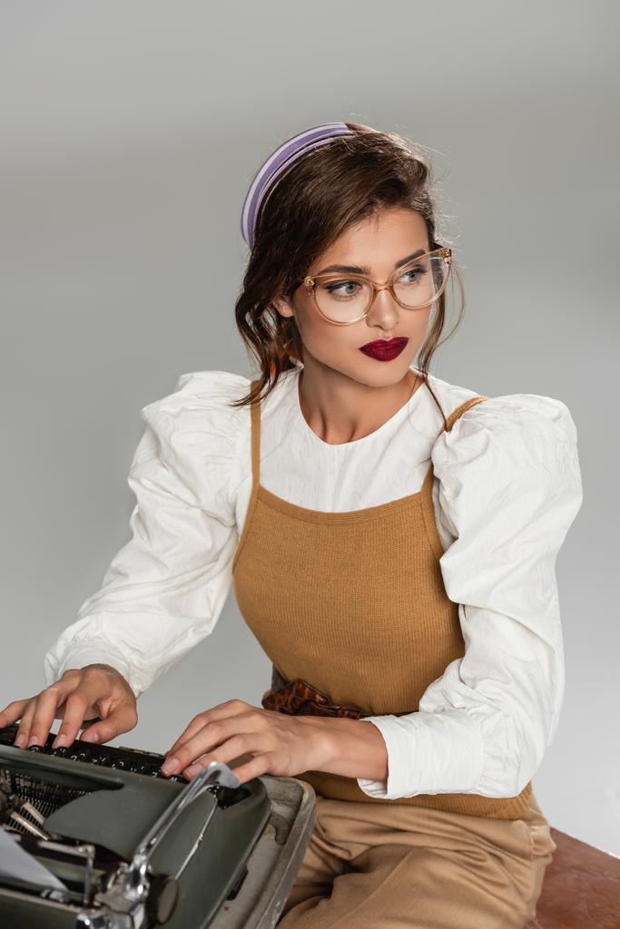 secretário da moda olhando embora enquanto digita em máquina de escrever vintage isolado em cinza - Foto, Imagem