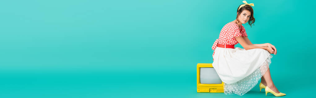 stylish pin up girl looking at camera while sitting on bright yellow retro tv on turquoise, banner - Photo, Image