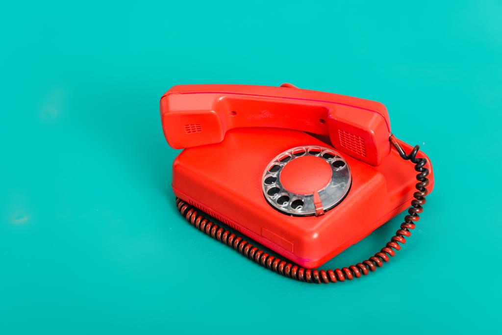 яскраво-червоний старовинний стаціонарний телефон на бірюзовому фоні
 - Фото, зображення