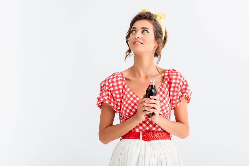glückliche Pin-up-Frau schaut weg, während sie eine Flasche Limo isoliert auf weiß hält - Foto, Bild