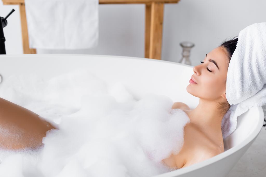 Молодая женщина в полотенце на голове принимает ванну  - Фото, изображение