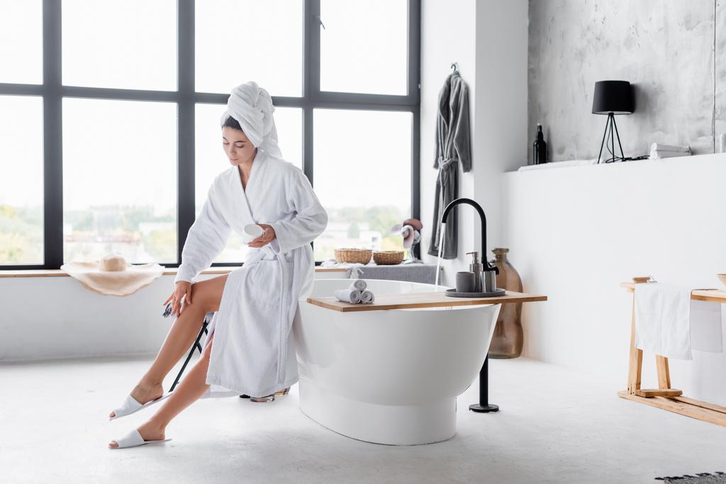 Frau trägt im Badezimmer kosmetische Creme auf Bein auf  - Foto, Bild