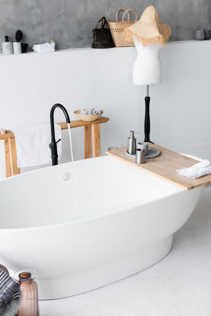 Туалетные принадлежности на деревянном подносе на ванне дома  - Фото, изображение