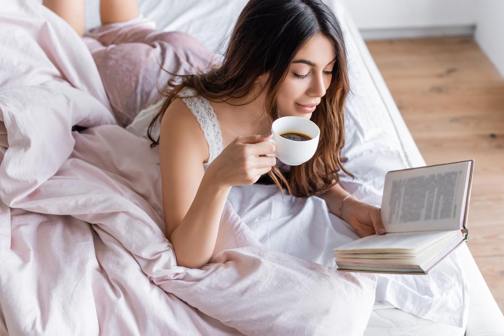 女性でpajama保持カップのコーヒーと読書本上のベッド  - 写真・画像