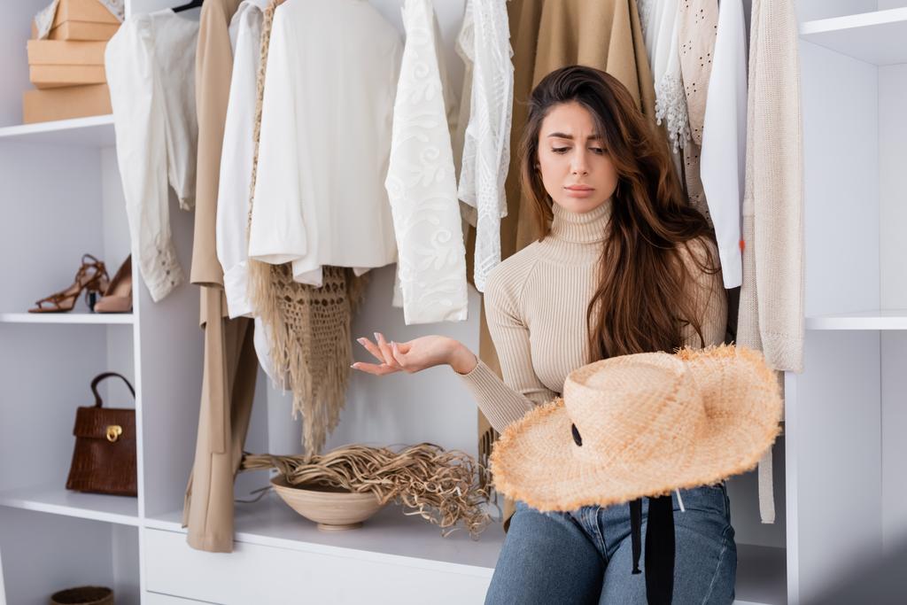 Woman holding sun hat near clothes in wardrobe  - Photo, Image